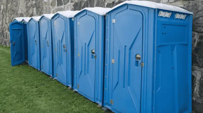 Row of blue portable toilets lined up on grass against a stone wall for event sanitation in Boston, MA