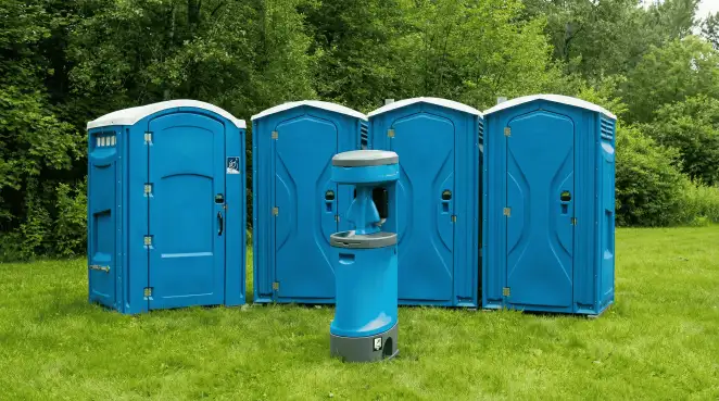 Four blue portable toilets and a matching hand washing station on grass near trees, a common sight at local outdoor events in Boston, MA