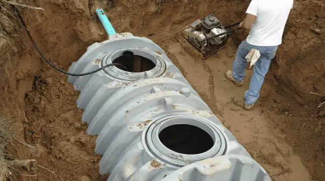 Septic tank installation showing a technician compacting soil around a new poly septic tank in an excavation pit in Boston, MA